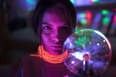 Close-up portrait of woman wearing illuminated necklace holding lighting equipment in darkroom