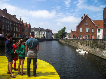 Rear view full length of family standing by river in city