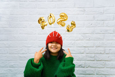 Happy asian baby girl in a green sweater close-up with golden balloons with numbers 2023 in hat