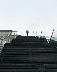 Low angle view of man climbing stairs against clear sky