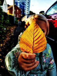 Close-up of girl holding autumn leaf while standing outdoors