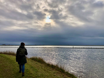 Rear view of woman walking by lake against sky