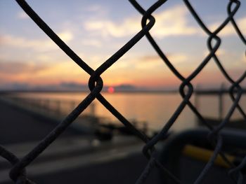 Close-up of chainlink fence against sky during sunset