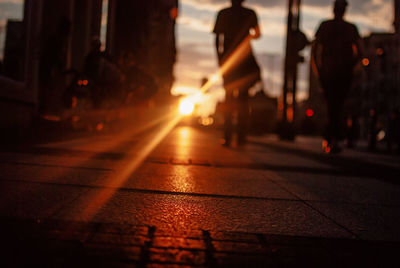 Surface level view of silhouette people walking on sidewalk in city during sunset