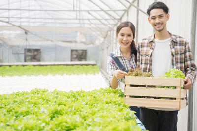 Portrait of smiling man and woman holding container with vegetable at farm