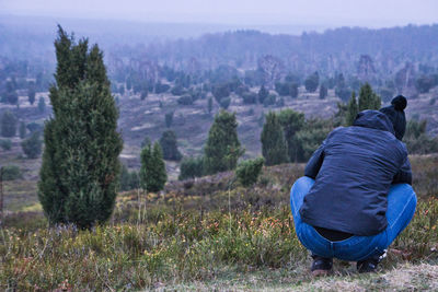 Rear view of man sitting on field against trees
