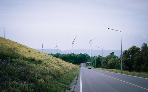 Road by wind turbines against sky