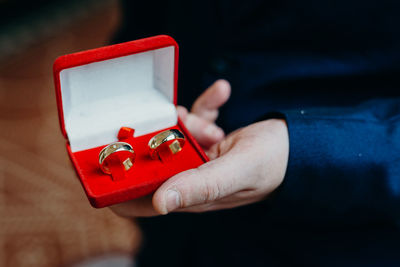 Low section of groom holding wedding rings while standing indoors