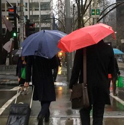 Rear view of people holding umbrella on sidewalk