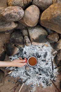 A woman's hand holds a red cup of coffee or tea by the fire during the hike