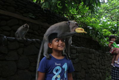 Monkey on boy shoulder eating banana by wall