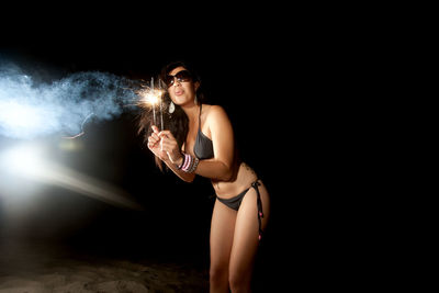 Woman in bikini playing with firework on beach at night