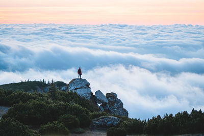 Man standing on rock against sky during sunset