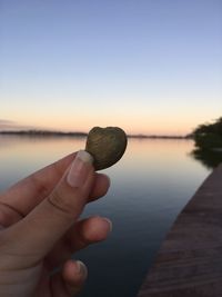 Midsection of person holding lake against sky during sunset 