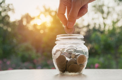 Close-up of hand holding coin over jar on table