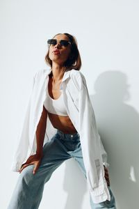 Young woman wearing sunglasses while standing against white background