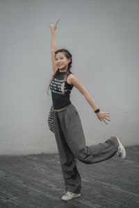 Portrait of young woman with arms raised standing against wall