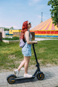 Young bright woman smiles and rides electric scooter in the summer in the city