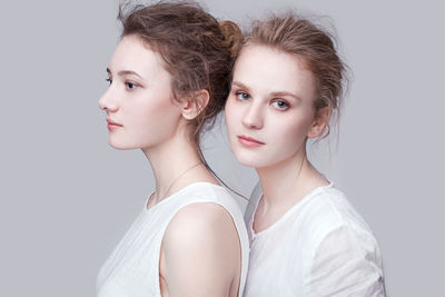 Portrait of young woman standing with thoughtful friend against white background