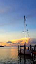 Sailboats moored in sea against sky during sunset