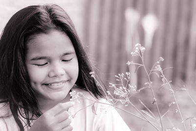 Cute smiling girl looking at flowering plant outdoors