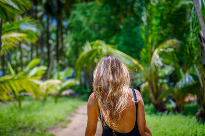 A young girl with blond long hair walks through a palm forest. high quality photo