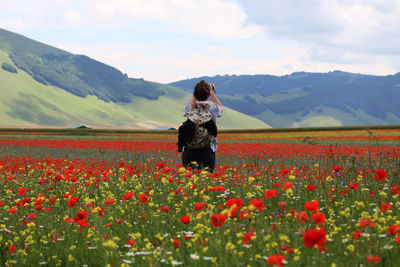 Rear view of woman standing amidst poppy field against sky