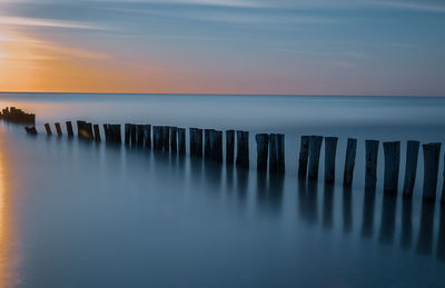 Wooden posts in sea against sky during sunset