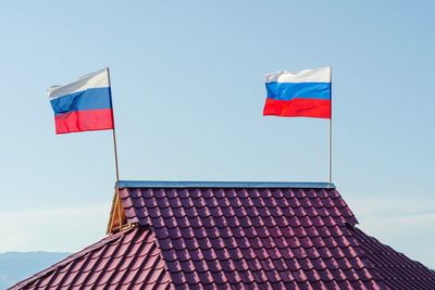 Two russian flags are developing on the roof of the house against the sky.