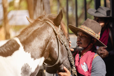 In an outdoor barn, one man dressed as a cowboy trains his horse to run in a circle around him.