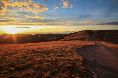 Road amidst field against sky during sunset