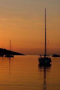 Sailboats sailing on sea against orange sky