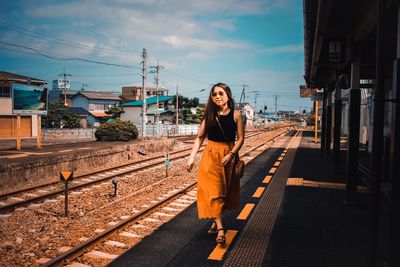 Young woman on railroad tracks against sky