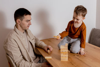 Father and son sitting together at home and playing with wooden blocks. jenga game. 
