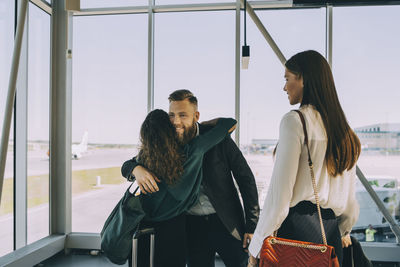 Smiling young businesswoman looking at colleagues greeting while standing in airport corridor