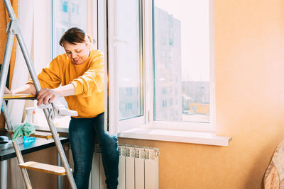 Mature woman sitting on window at home