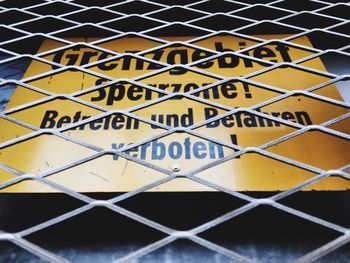 Low angle view of warning sign seen through chainlink fence