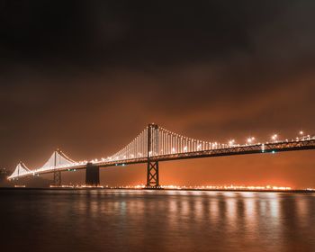 Illuminated bridge over river against sky at night