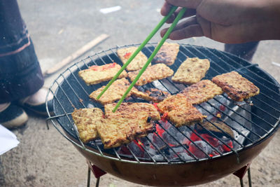 Cropped hand preparing meat on barbecue grill