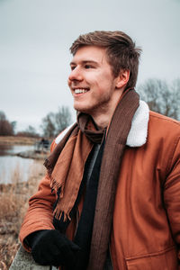 Smiling young man looking away while standing against sky