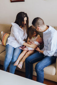 Older sister holding her newborn baby brother next to their parents on the sofa