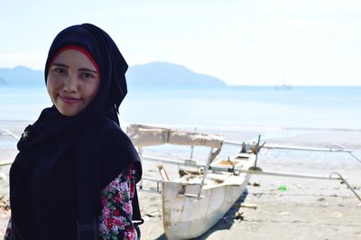 Portrait of smiling young woman standing at beach against sky