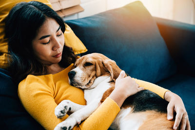 Young woman with dog sitting on sofa at home