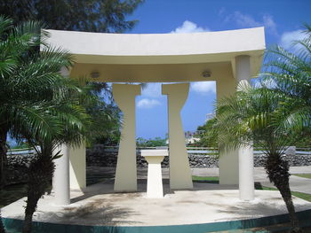 Gazebo by palm trees and building against sky