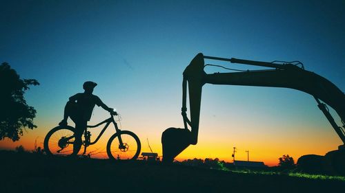 Silhouette man with bicycle by bulldozer during sunset