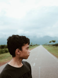 Portrait of young man standing in the middle of a straight road against sky