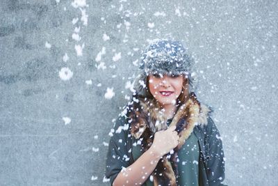 Snow falling against woman standing by wall
