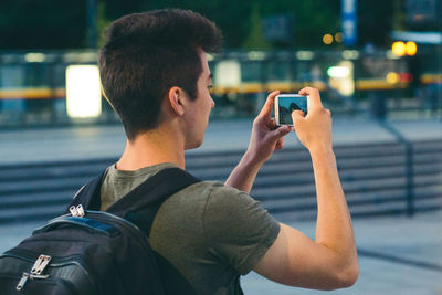 Rear view of man photographing with mobile phone in city