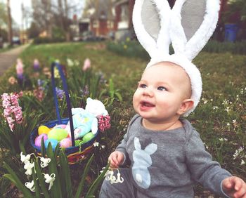 Happy baby boy wearing rabbit headband while sitting in park during easter