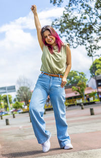 Young woman with one hand raised and smiling in park